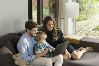 Smiling parents and son sitting on sofa using laptop at home