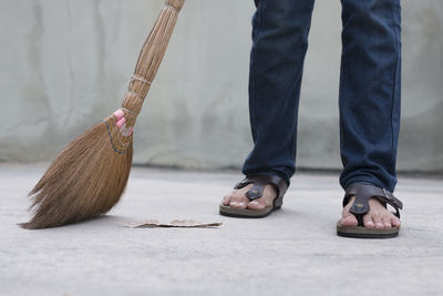 Low section of man sweeping footpath with broom against wall