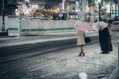 People with umbrellas standing on snow in city