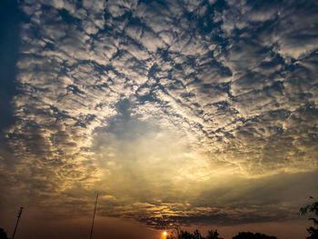 Low angle view of sunlight streaming through clouds during sunset