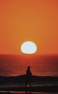 Silhouette person standing by sea against orange sky