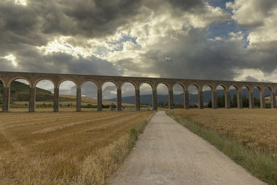 Arch bridge on field against sky