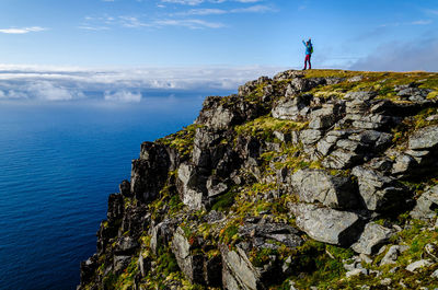 Rear view of man standing on cliff by sea against sky