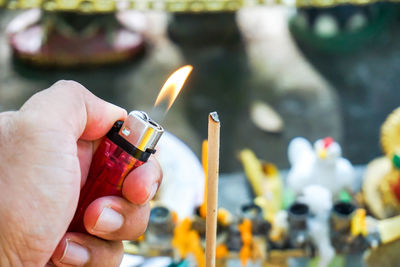 Cropped image of hand burning incense stick with lighter
