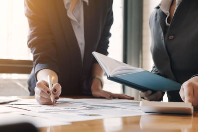 Midsection of woman holding paper while standing on table