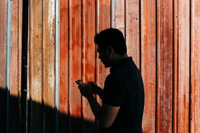 Side view of man using mobile phone against rusty metal