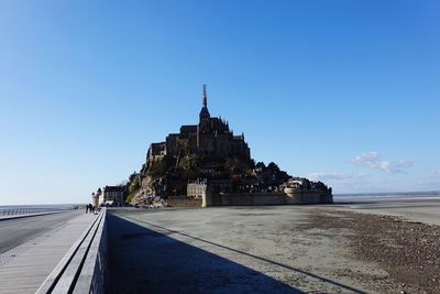 Silhouette building by sea against clear blue sky during sunny day