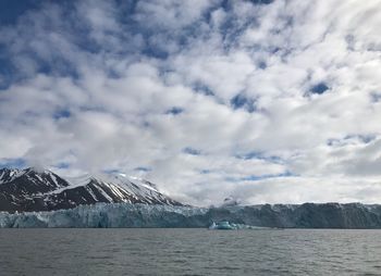 Scenic view of sea by snowcapped mountains against sky