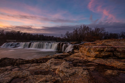 Scenic view of waterfall against sky during sunset