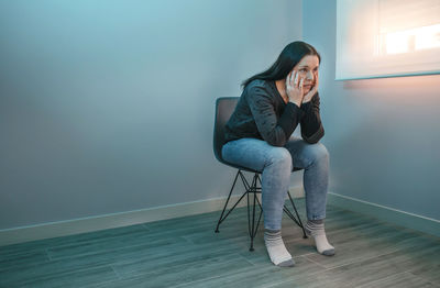 Depressed woman sitting on chair sitting against wall