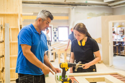 Male instructor teaching female trainee at workbench in illuminated workshop