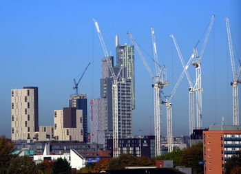 Low angle view of cranes and buildings against clear blue sky