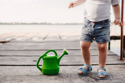 Low section of boy standing by watering can outdoors