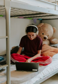 A teenage girl sits on a bed with a computer.