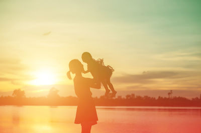 Side view of silhouette woman standing on shore against sky during sunset