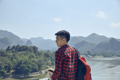 Young man looking at mountains against sky