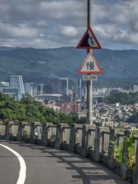 Road sign by buildings against sky in city