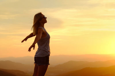 Rear view of woman standing against sky during sunset