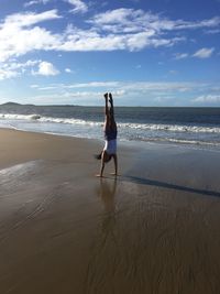 Full length of woman practicing handstand at beach