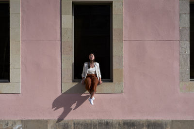 Young woman sitting on window sill of building during sunny day