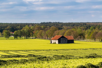 House on field by trees and houses against sky