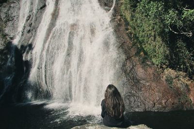 Rear view of woman looking at waterfall in forest