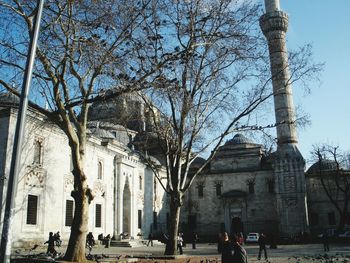 Bare trees in front of temple against sky