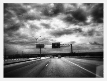 Cars moving on road against cloudy sky