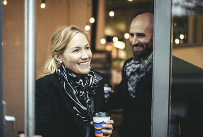 Smiling mid adult businesswoman and businessman leaving cafe