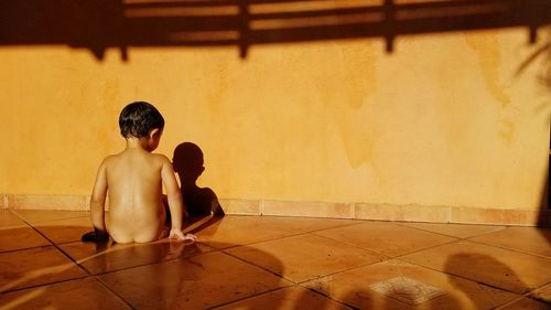 Rear view of naked boy sitting on floor at home