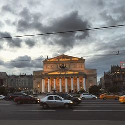 Traffic on road in city against cloudy sky