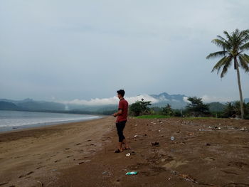 Rear view of man standing on beach against sky