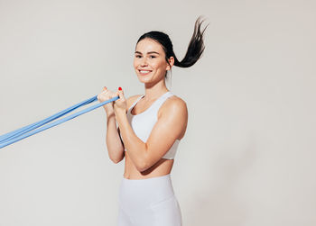 Portrait of young woman with arms raised standing against white background