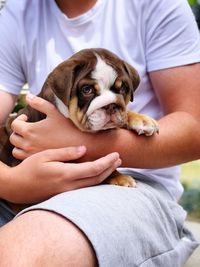 Midsection of man holding dog while sitting outdoors