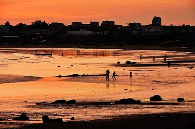 People at beach against sky during sunset
