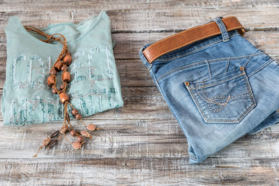 High angle view of top and necklace by jeans on wooden table
