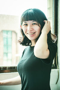 Portrait of smiling young woman standing against window