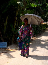Woman carrying umbrella walking with son on footpath by plant