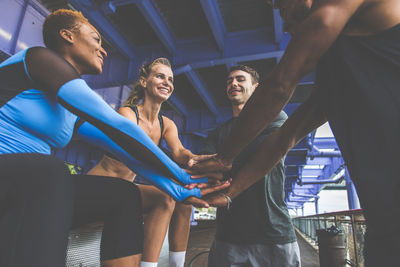 Friends stacking hands while standing under bridge