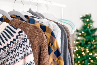 Knitted sweaters on hangers on clothes rack in the shop with blurred christmas tree background.