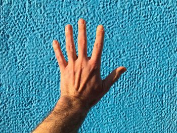 Cropped hand reaching towards blue wall