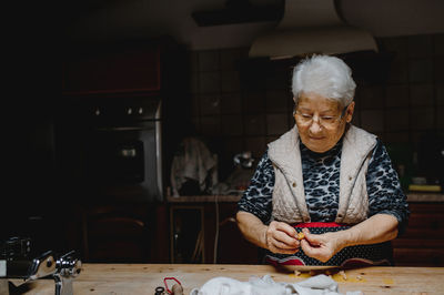 Aged housewife preparing delicious homemade tortellini while standing at table in kitchen at home