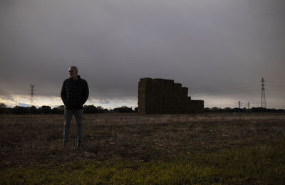 Adult man in winter clothes in fields with group of straw bales