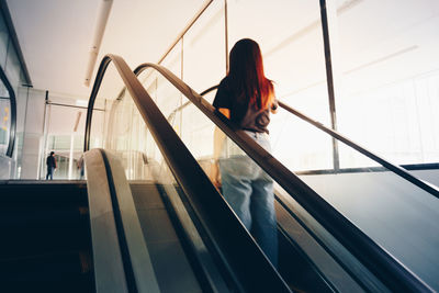 Rear view of woman standing on escalator