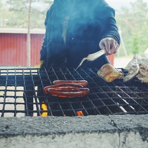 Midsection of man grilling sausages on barbecue at forest
