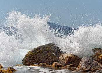 A wave breaks on big stones in the water, thousands of drops of water sparkle in the sunlight