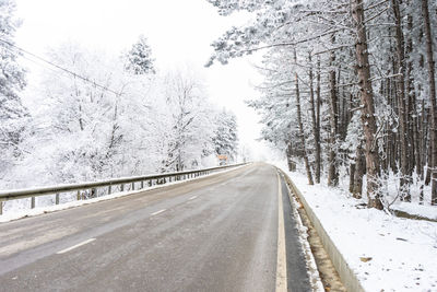 Snow covered road amidst trees during winter