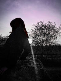 Side view of woman on field against sky during sunset