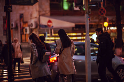 Rear view of people walking on street in city at night