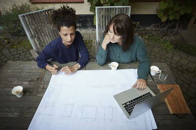 High angle view of female engineers discussing over blueprint at table in backyard